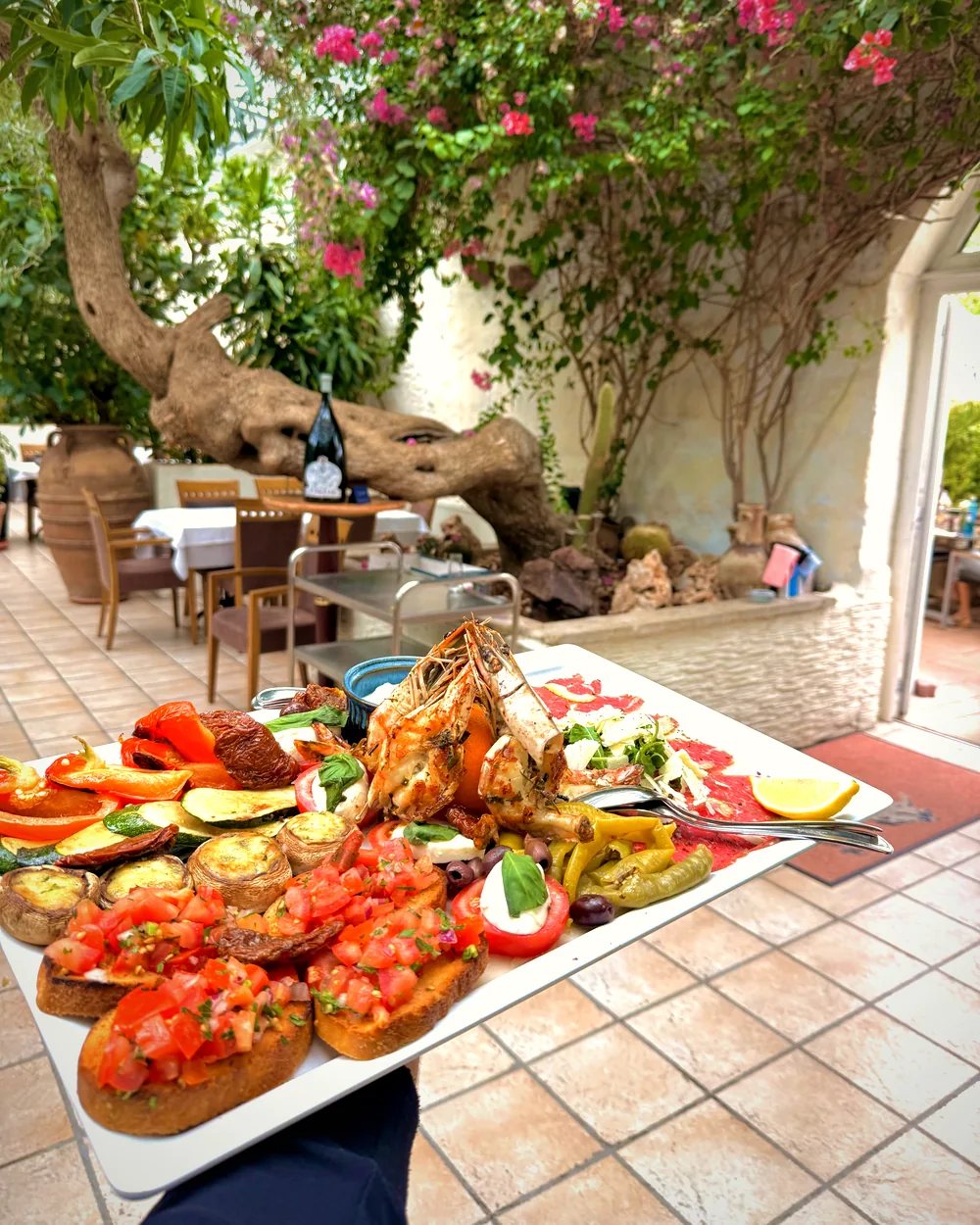 Gemischte Antipasti-Platte, im Hintergrund die Terrasse mit altem Olivenbaum
