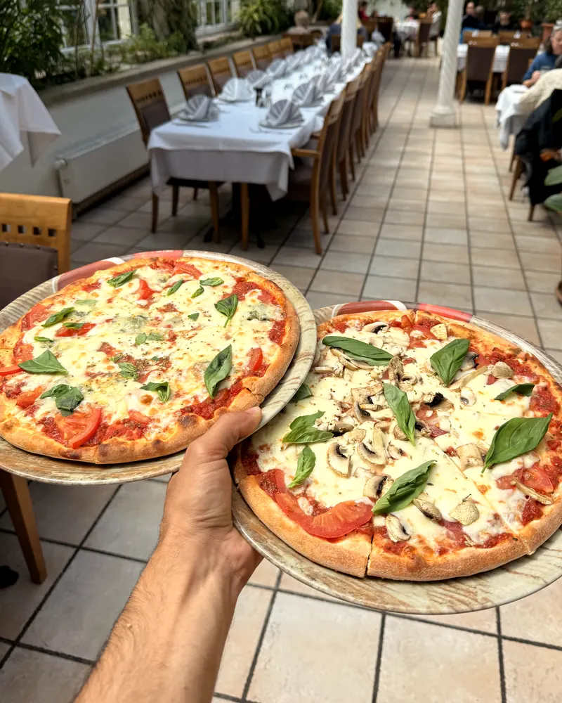 Zwei frisch gebackene Pizzen, Margherita und mit Champignons, in der Hand gehalten